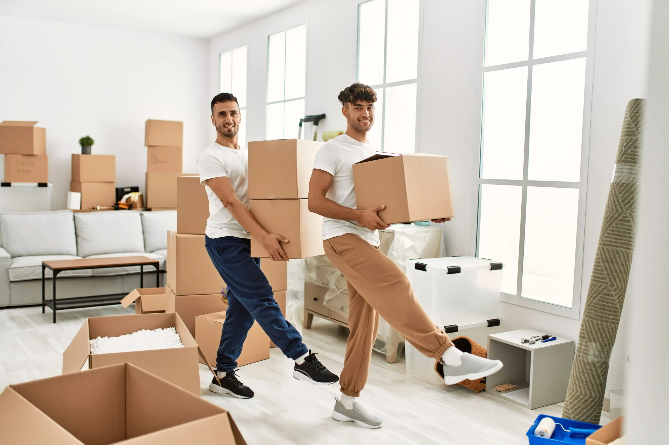 Two hispanic men couple smiling confident holding cardboard boxes new home 1 scaled